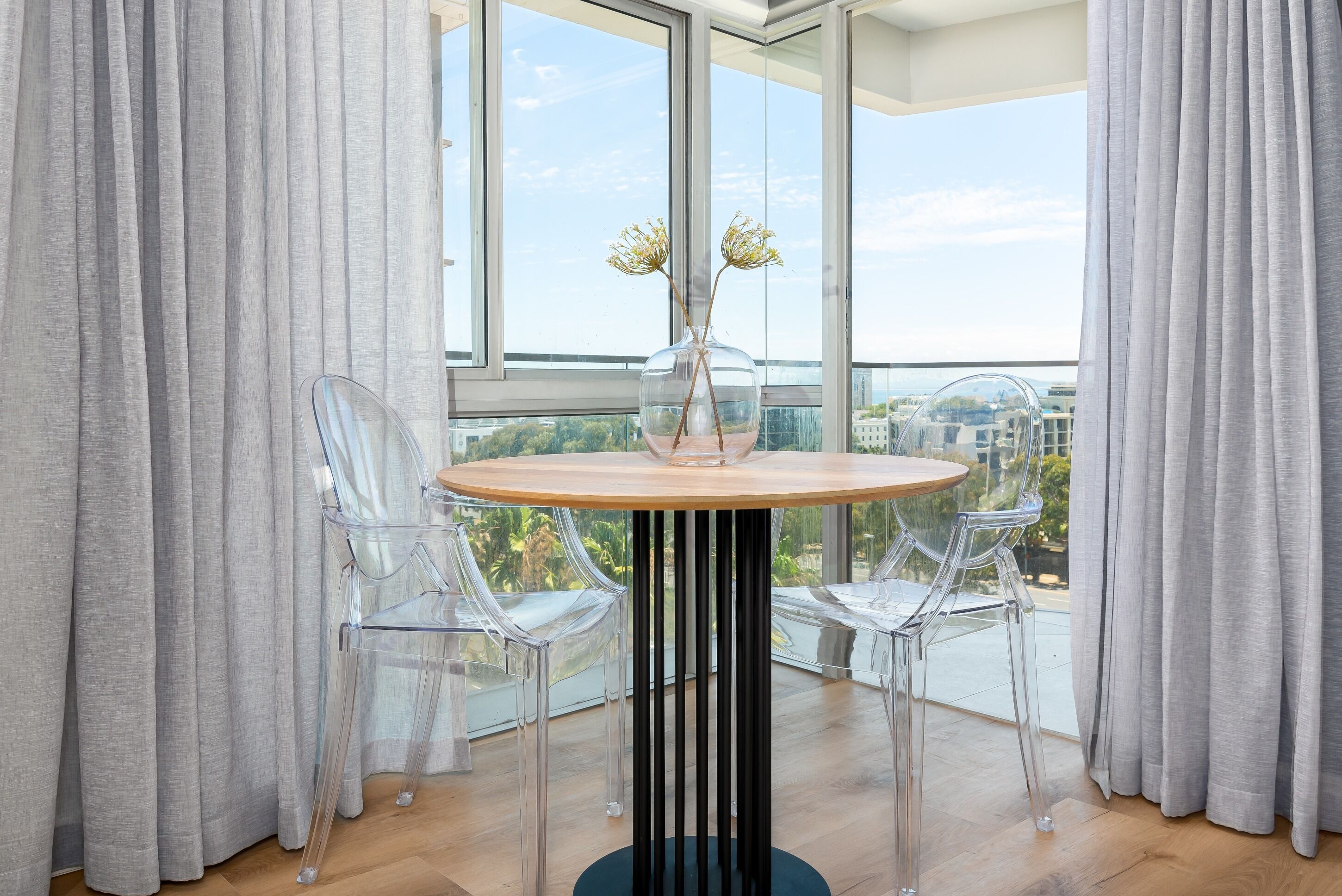 A modern dining area with a round table, two clear chairs, and a vase with flowers.