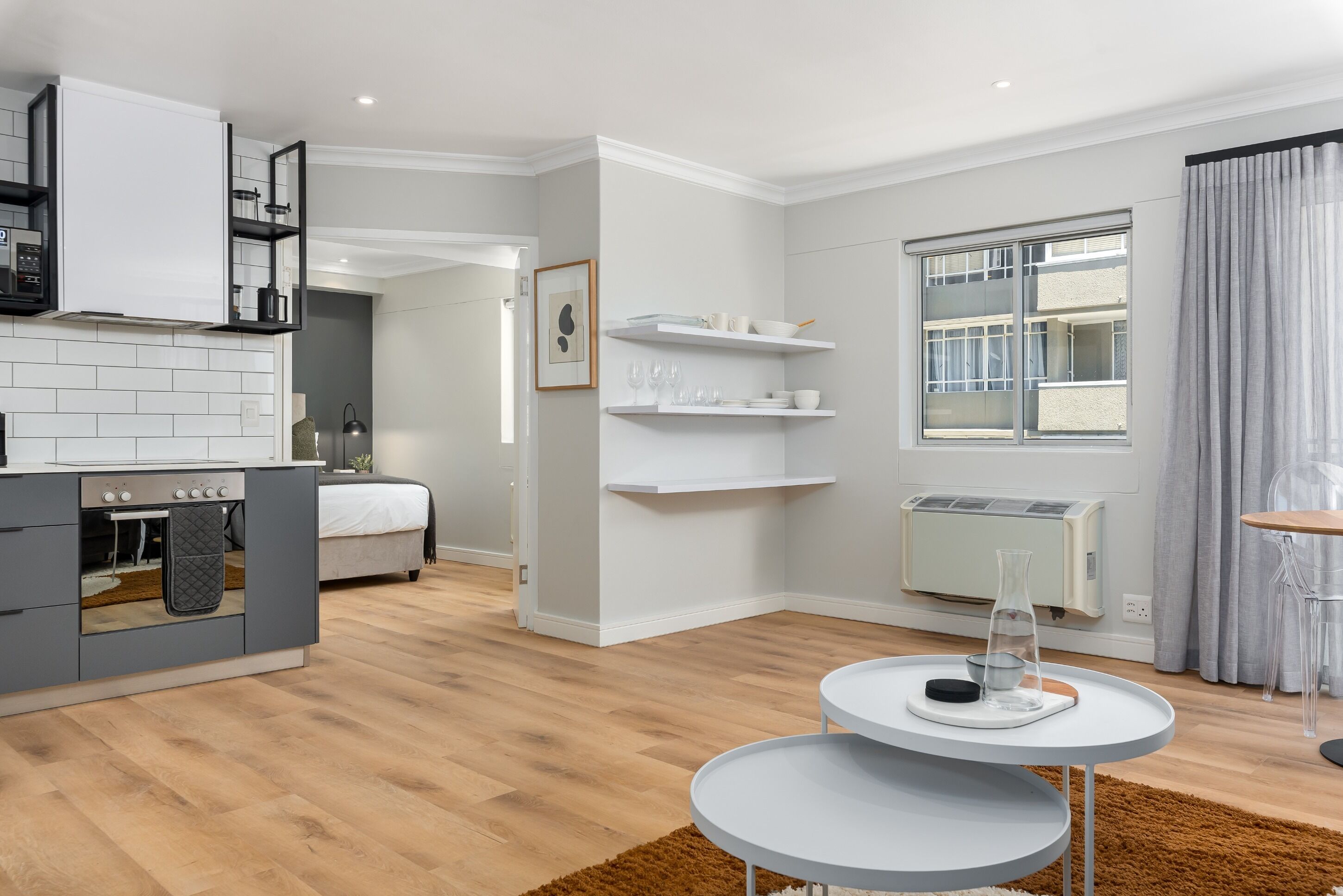 A modern kitchen with grey cabinets, a built-in oven, and a dining area with a round table and chairs.