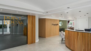 Una moderna zona de recepción con un mostrador de madera, una puerta de cristal y un área de descanso con una silla.
