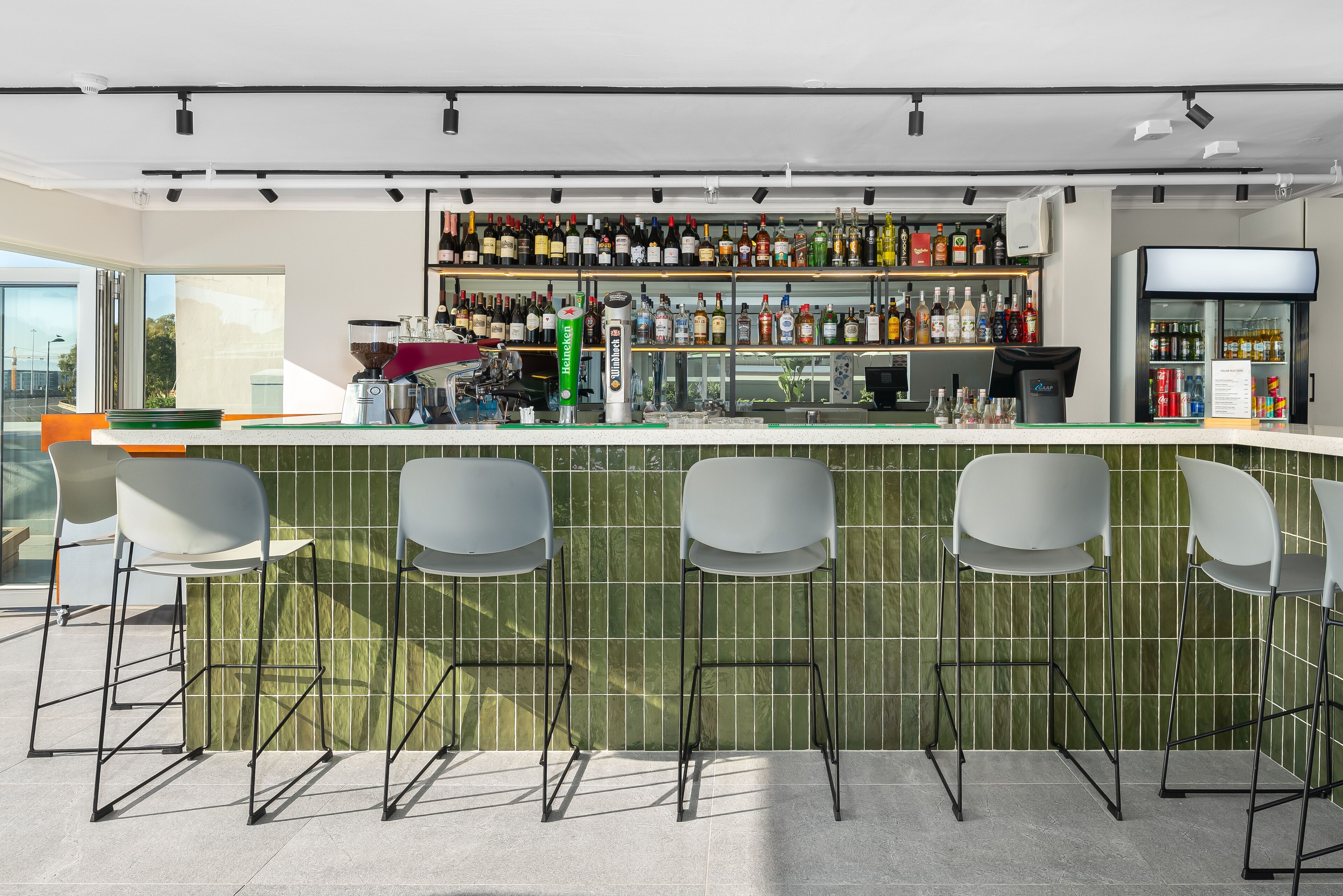 Eine moderne Bar mit einer langen Theke, mehreren Barhocker und einer Auswahl an Spirituosen.