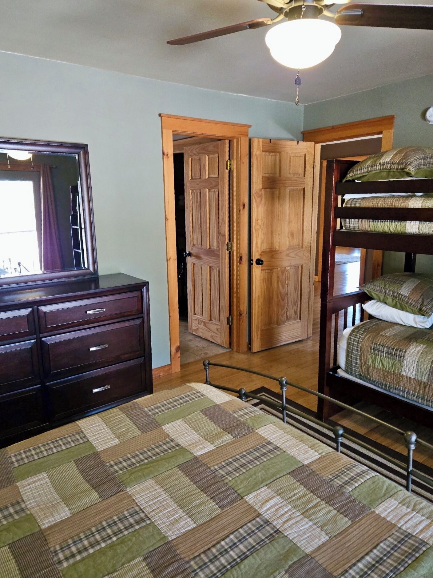 Een slaapkamer met een houten dressoir, een geborduurde spreidekbed en een stapelbed, plus een plafondventilator.