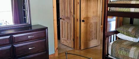 Een slaapkamer met een houten dressoir, een geborduurde spreidekbed en een stapelbed, plus een plafondventilator.