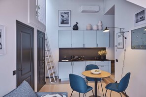 Una cocina moderna con armarios blancos, una mesa redonda de comedor con sillas azules y una escalera que conduce a un nivel superior.