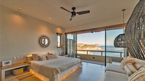 A bedroom with a large bed, a sofa, a ceiling fan, and a view of the ocean. - Ocean View Penthouse with Rooftop Terrace (Huatulco)