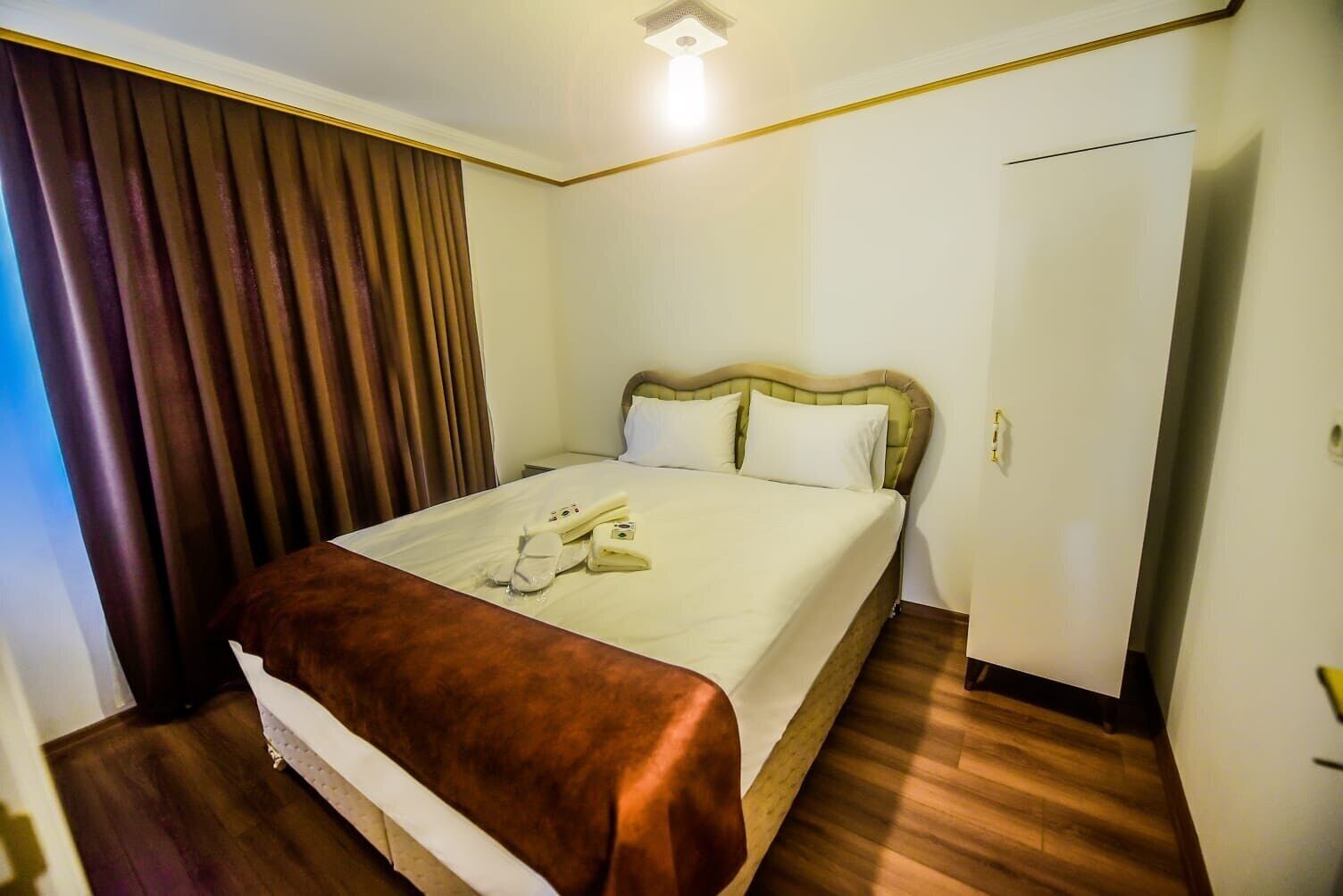 Ein Hotelzimmer mit Bett, Nachttisch, Kleiderschrank und Vorhang.