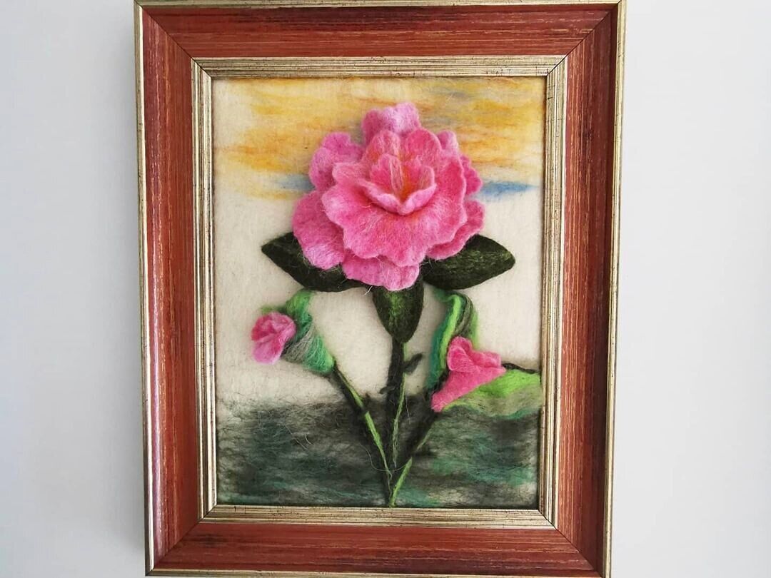 A framed artwork of a pink flower with green leaves.