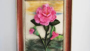 A framed artwork of a pink flower with green leaves.
