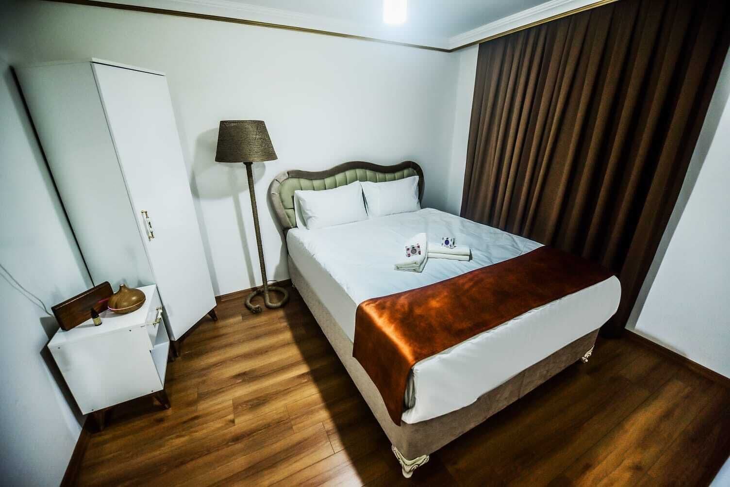A hotel room with a bed, a bedside table, a lamp, and a curtain.