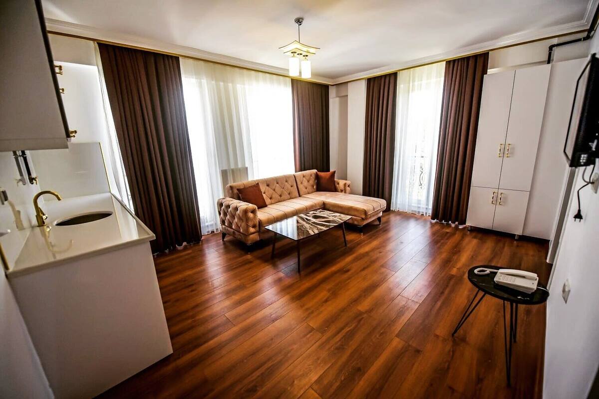 A modern living room with a sofa, a coffee table, and a small side table. There is a white cabinet with a gold faucet, and a television mounted on the wall.