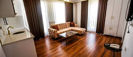 Una sala moderna con un sofá, una mesa de centro y una mesita auxiliar. Se observa un armario blanco con un grifo dorado, y un televisor montado en la pared.