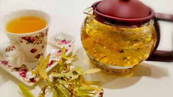 Una tetera y una taza con diseños florales, sobre una superficie blanca con hojas y tallos de té.