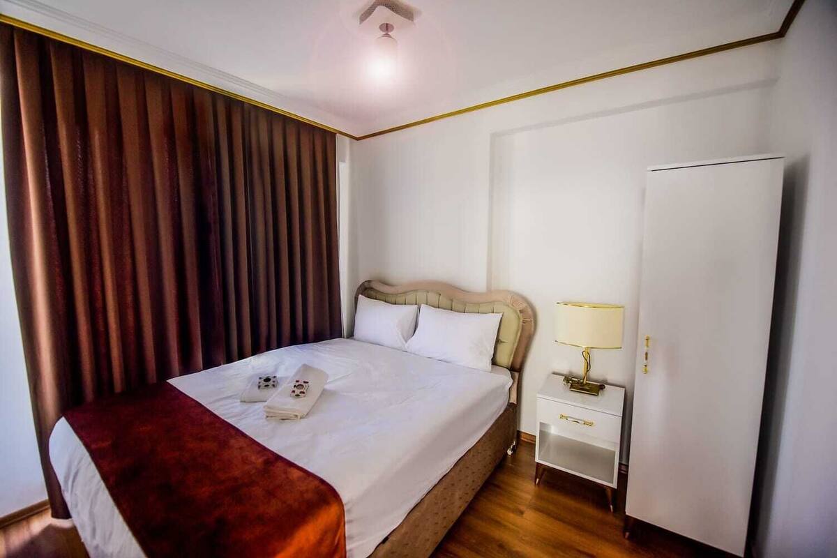 A hotel room with a bed, a nightstand with a lamp, a wardrobe, and a window with curtains.