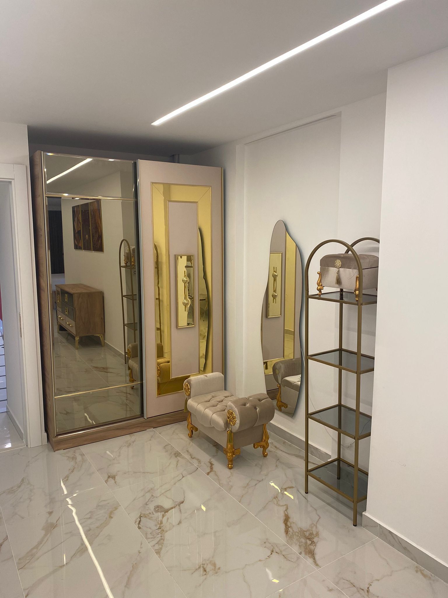Una habitación con piso de mármol, un armario espejado, una tocador con espejo y una silla con marco dorado.