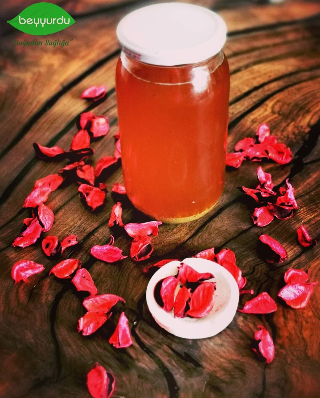Un bocal de líquid vermell amb tapa blanca, envoltat de pètals vermells sobre una superfície de fusta.
