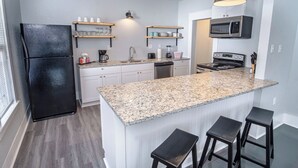 Una cocina moderna con encimera de granito, refrigerador negro, electrodomésticos de acero inoxidable y taburetes de bar.