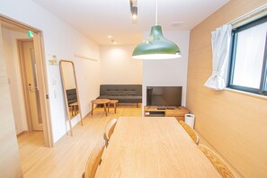 A modern room with a wooden dining table, a sofa, a TV, and a large window with curtains.