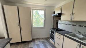Een moderne keuken met een ingebouwde kookplaat, oven en gootsteen. Een raam zorgt voor natuurlijk licht en uitzicht op bomen.