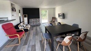 Een moderne woonkamer met een eethoek, met een zwarte eettafel, rode en bruine stoelen, een grijze bank en een boekenkast.