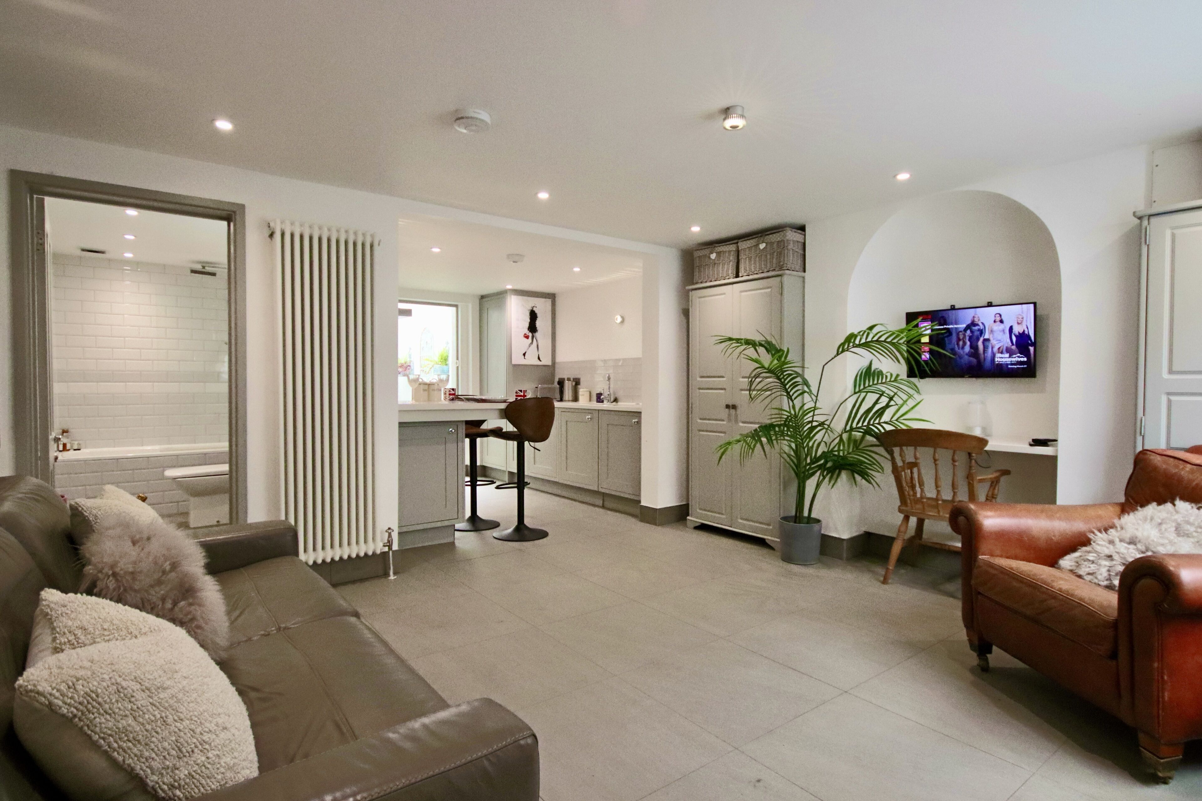 A modern living room with a brown leather sofa, a brown leather armchair, and a television mounted on the wall.