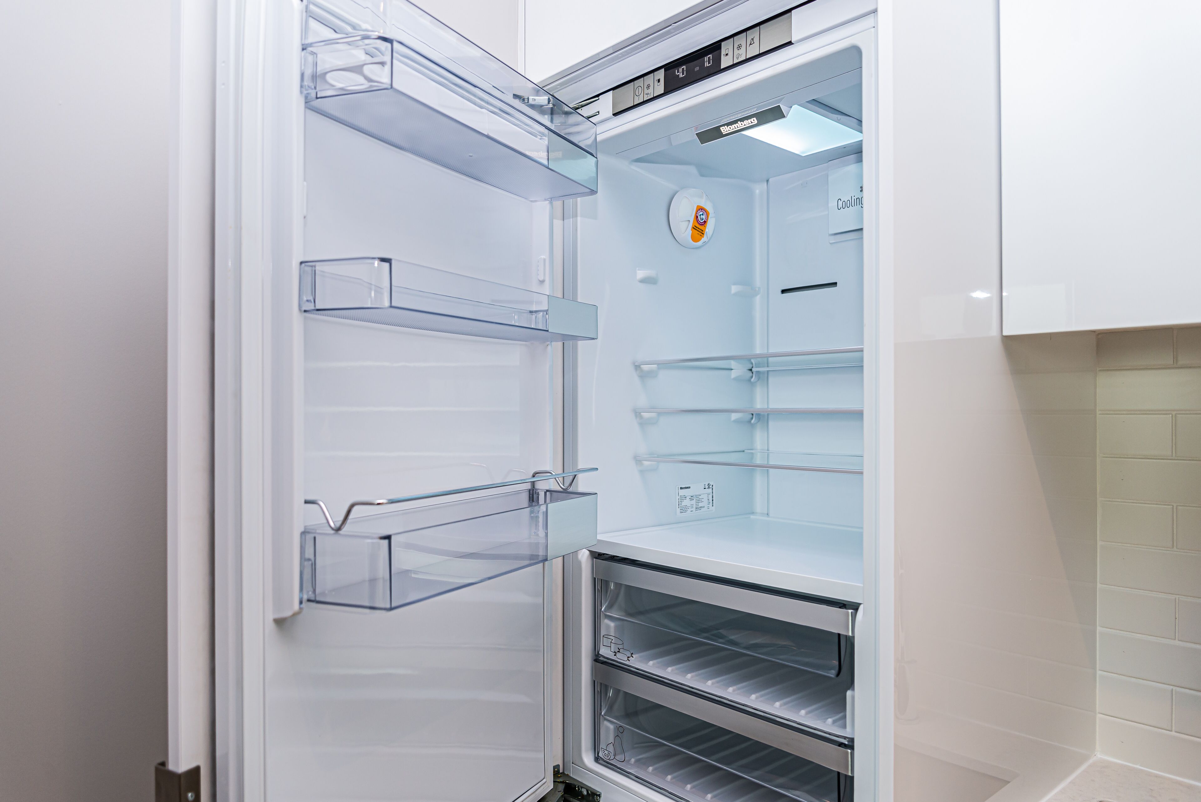 Un refrigerador moderno y vacío con varias estantes y una pantalla digital.