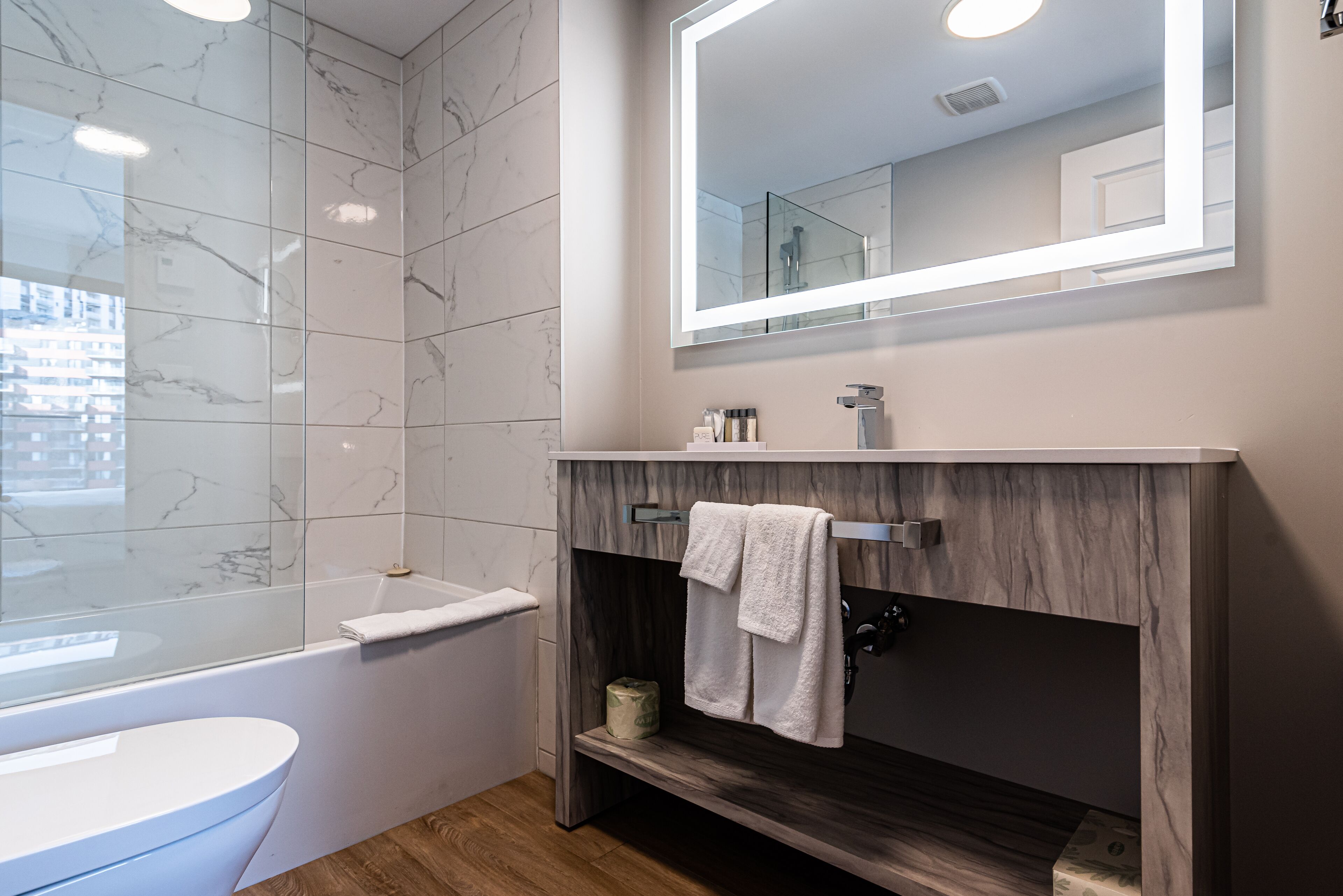A modern bathroom with a marble-tiled shower, a white sink, and a vanity with a mirror.