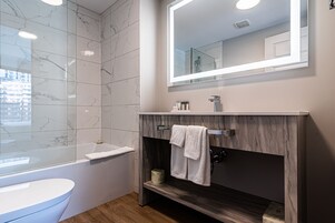 A modern bathroom with a marble-tiled shower, a white sink, and a vanity with a mirror.
