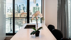 Uma cozinha moderna com uma janela ampla, uma orquídea em vaso e vista para o horizonte urbano.