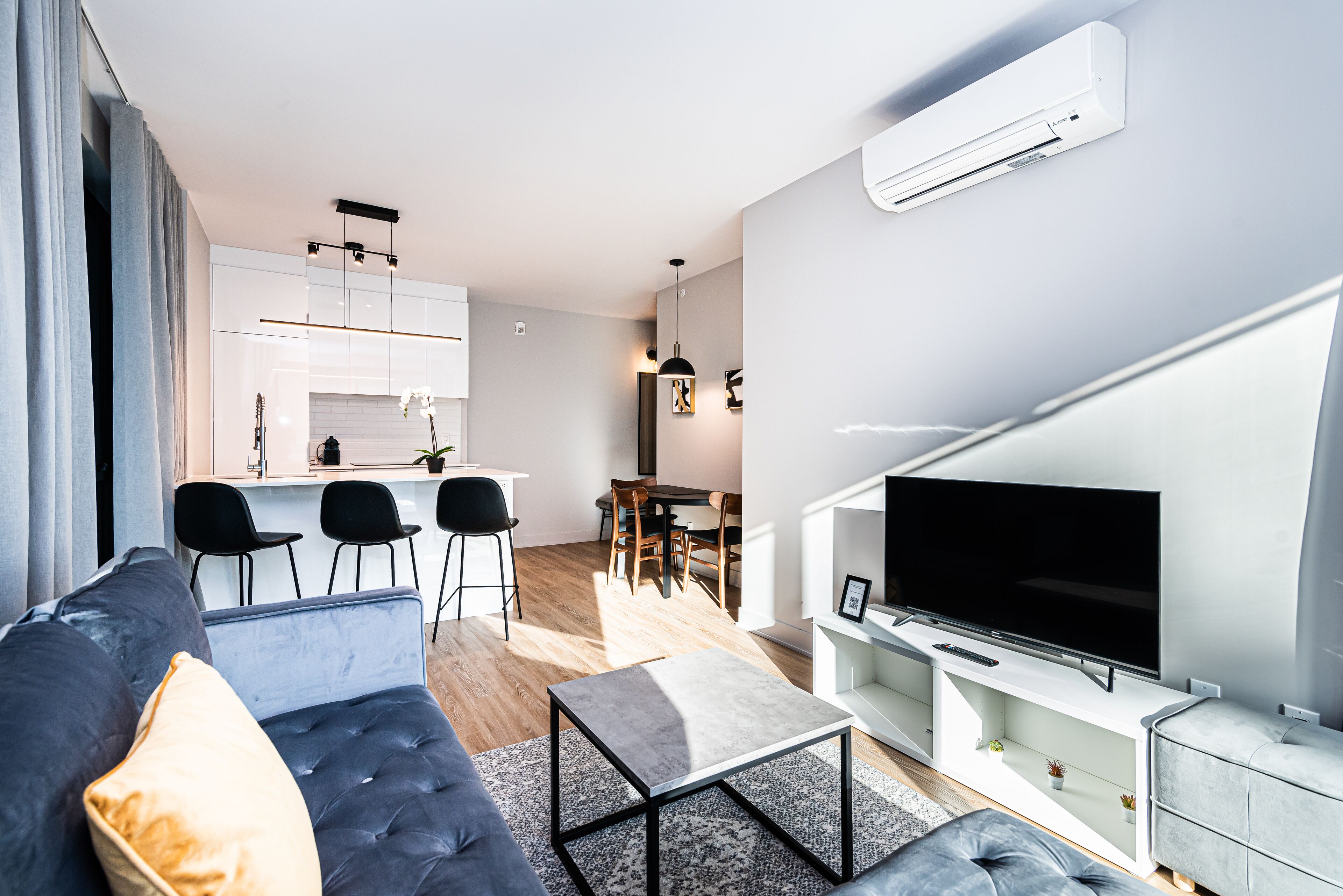 Un soggiorno moderno con divano, tavolino da caffè e TV. Si intravede una cucina con zona pranzo sullo sfondo.
