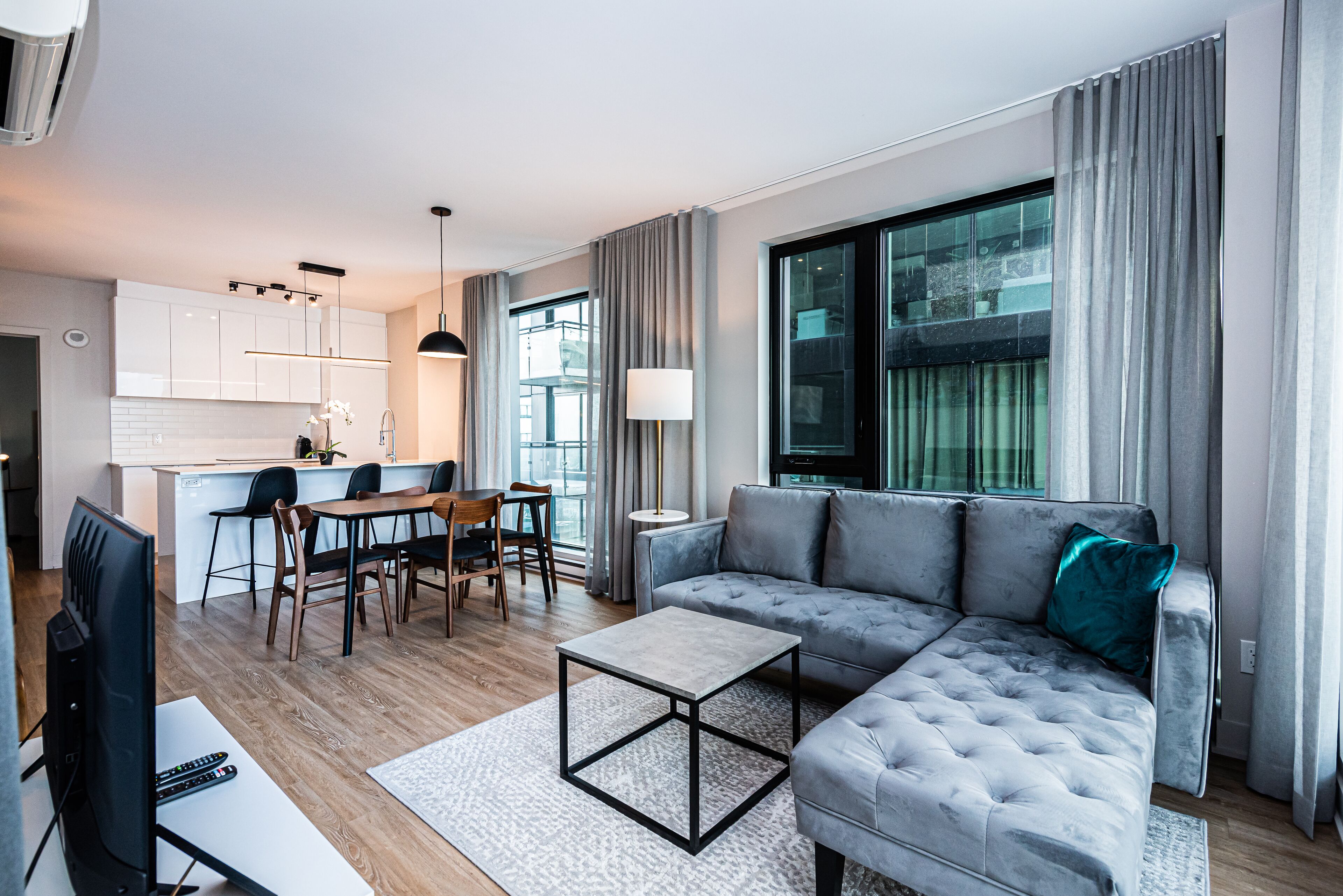 A modern living room with a grey sectional sofa, a coffee table, and a dining area with a table and chairs.