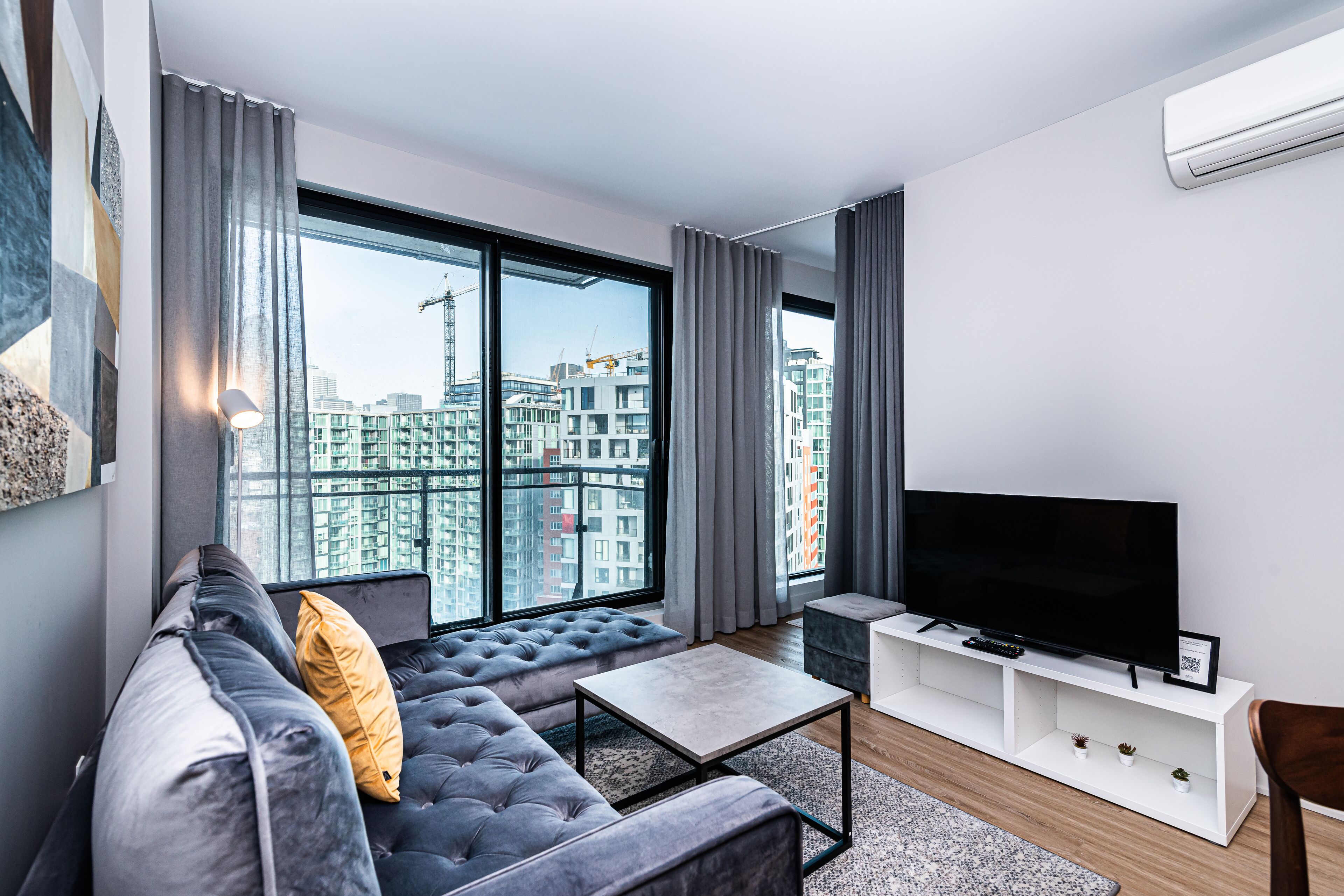 Ein modernes Wohnzimmer mit einem großen Fenster, einem Sofa, einem Couchtisch und einem Fernsehgerät auf einem weißen Schrank.