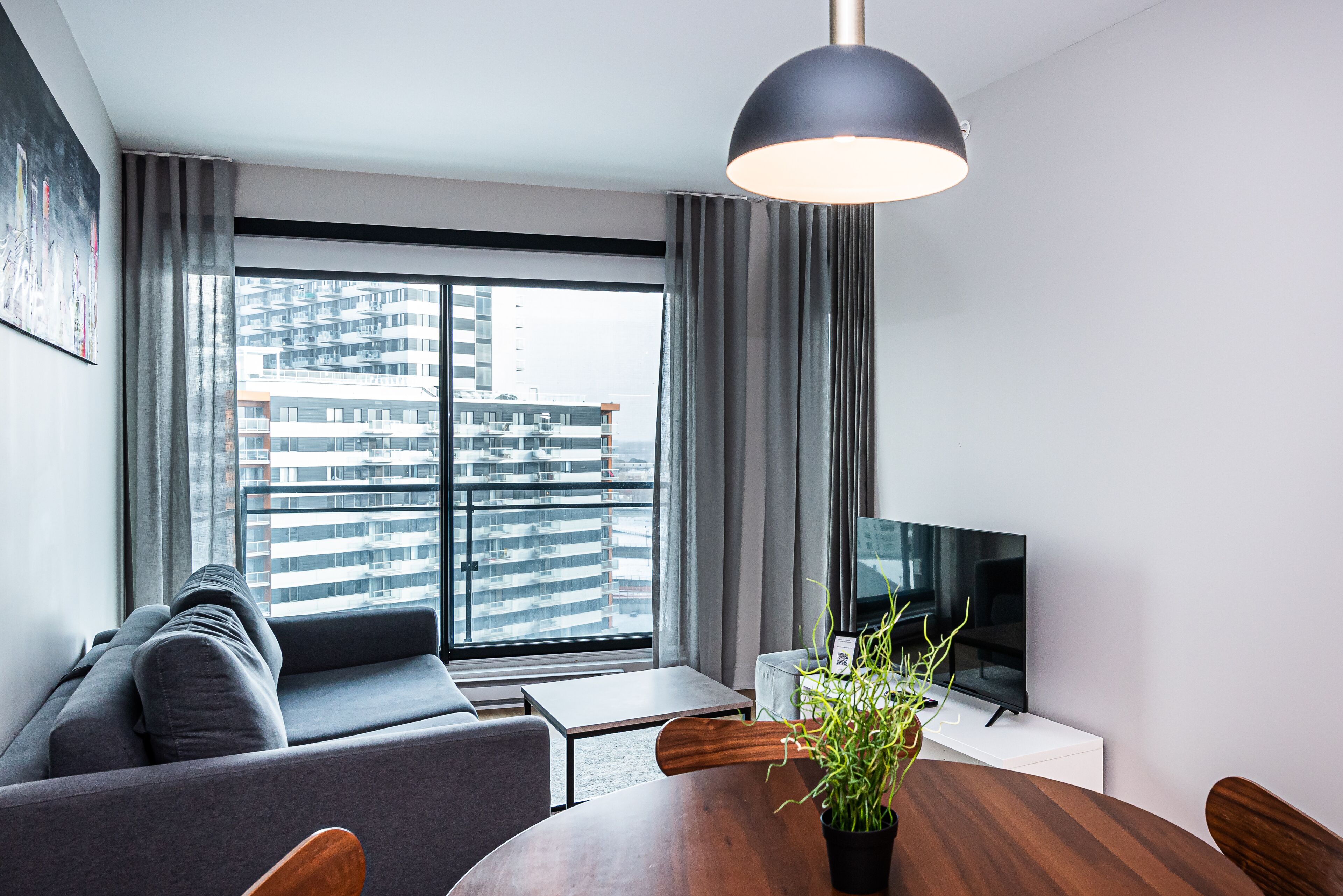 Una sala de estar moderna con sofá, mesa de comedor, televisor y un ventanal con vista a la ciudad.