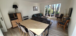 A spacious living area with a wooden dining table, grey sofas, and wicker chairs.