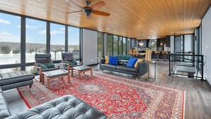 A spacious living area with a large window, a ceiling fan, and a red patterned rug. - Modern 4 bd, 3 bath Cottage on Boshkung Lake, Haliburton (Algonquin Highlands)