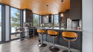 A modern kitchen with wooden ceiling, large windows, and bar stools. - Modern 4 bd, 3 bath Cottage on Boshkung Lake, Haliburton (Algonquin Highlands)