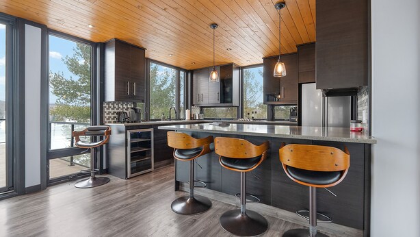 A modern kitchen with wooden ceiling, large windows, and bar stools. - Modern 4 bd, 3 bath Cottage on Boshkung Lake, Haliburton (Algonquin Highlands)