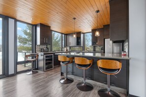 A modern kitchen with wooden ceiling, large windows, and bar stools. - Modern 4 bd, 3 bath Cottage on Boshkung Lake, Haliburton (Algonquin Highlands)
