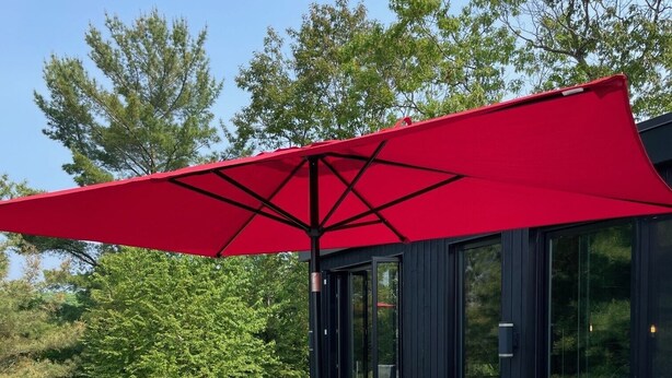 An outdoor seating area with wicker furniture and red cushions, a glass table, and a red umbrella. - Modern 4 bd, 3 bath Cottage on Boshkung Lake, Haliburton (Algonquin Highlands)