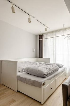 Quarto moderno e minimalista com cama, gavetas embutidas e luminária no teto.