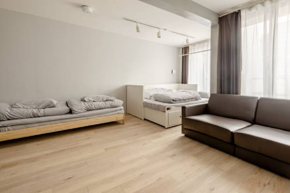 Quarto moderno e minimalista, com piso de madeira, um sofá e duas camas com roupa de cama cinzenta.