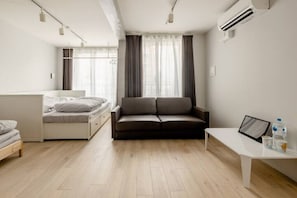 Quarto moderno e minimalista com cama, sofá e uma pequena mesa com porta-retrato e garrafas de água.