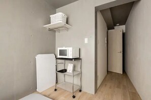 A compact kitchen with a microwave, a small fridge, and a metal cart with shelves.