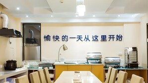 A modern dining area with a long table, chairs, and kitchen appliances. - City Comfort Inn (Hezhou)