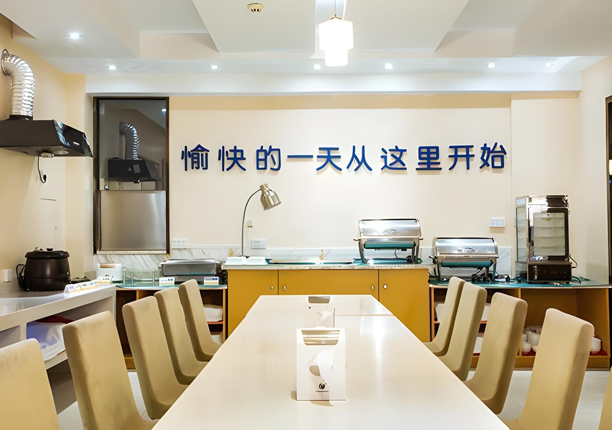 A modern dining area with a long table, chairs, and kitchen appliances.