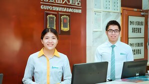 A reception desk with two staff members, a signboard with the hotel name, and certificates on the wall. - City Comfort Inn (Hezhou)