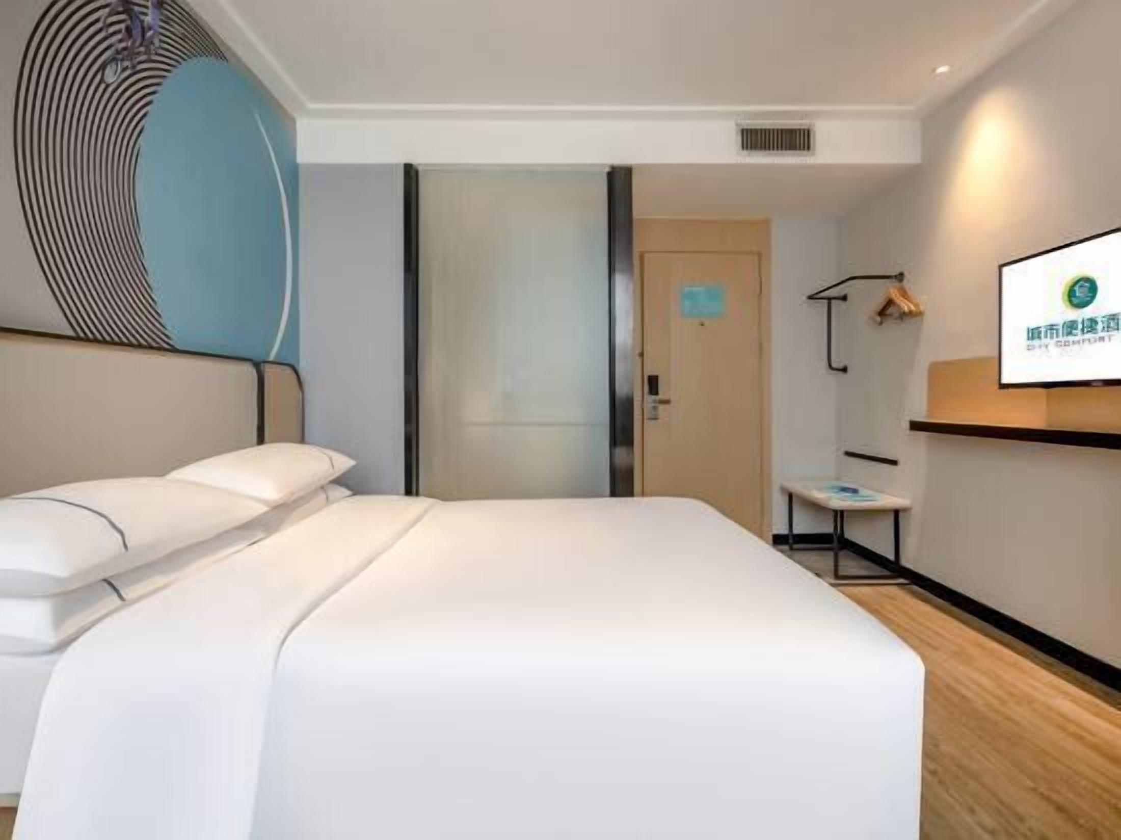 A modern hotel room with a large bed, a bedside table, a TV, and a door leading to another room.