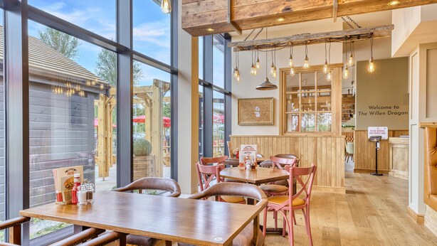 A restaurant interior with large windows, wooden tables, and chairs. - Premier Inn Milton Keynes - Willen Lake (Milton Keynes)