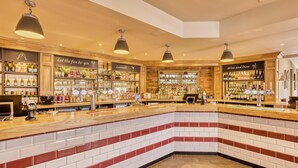 A bar area with shelves of alcohol, a counter with a cash register, and hanging lights. - Premier Inn Milton Keynes - Willen Lake (Milton Keynes)