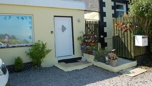 Una casa con puerta blanca, un pequeño porche con plantas en macetas y una valla de madera con adornos coloridos.