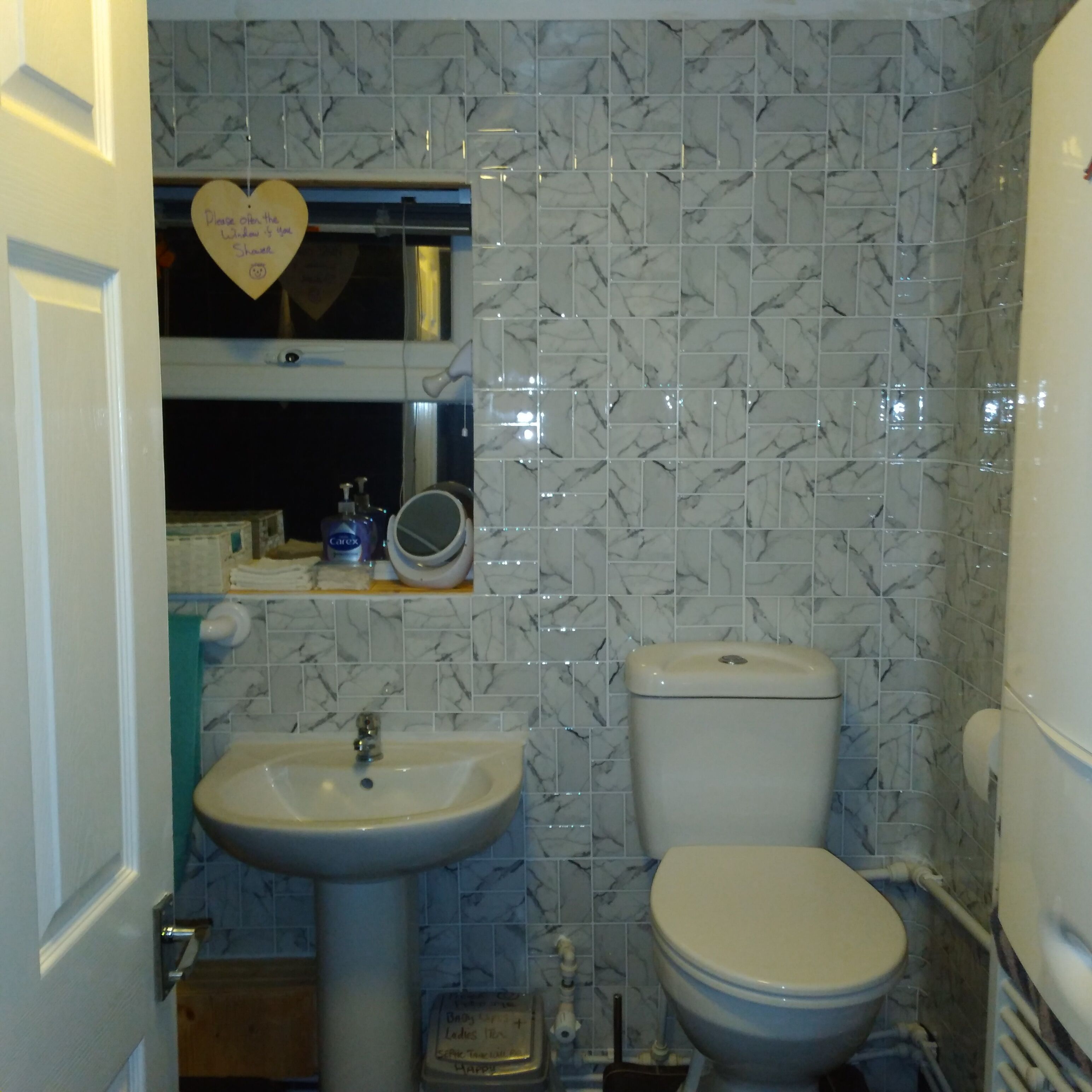 Ein Badezimmer mit einem weißen Waschbecken, Toilette und einem Spiegel über dem Waschbecken. Die Wände sind mit einem Marmormuster gefliest.