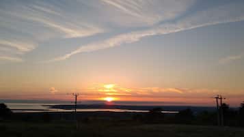 Un coucher de soleil sur une étendue d’eau, avec une côte lointaine, des lignes électriques et des arbres.